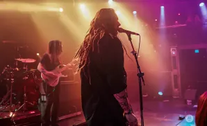 A rock band performs on a dimly lit stage with colorful spotlights.