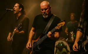 A band plays on stage, with a bassist in the foreground and singers and drummer behind.