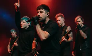 A band performs on stage with red and blue lighting. The lead singer sings into a microphone.