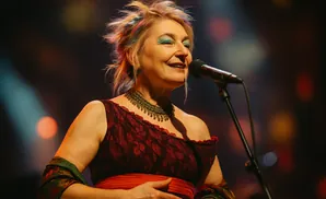 A woman with colorful hair sings into a microphone on stage.