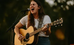 A woman sings passionately into a microphone while playing an acoustic guitar.