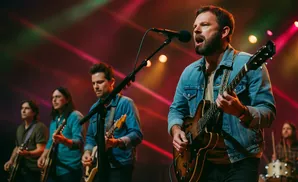 A band performs on stage with dramatic lighting, with a lead singer in the foreground playing a guitar.