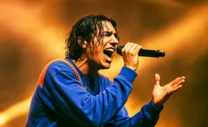 Singer with wet hair and open mouth sings into microphone, wearing a blue sweatshirt.