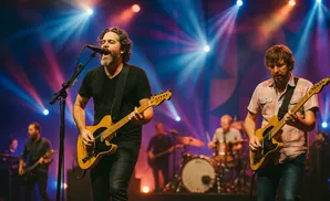 A lead singer and guitarist perform on stage with a band, bathed in blue and red stage lights.