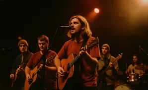 A band performs on stage with a lead singer playing guitar and singing into a microphone, backed by other musicians.