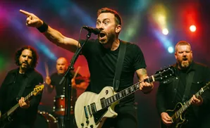 A band performs on stage with colorful lights, featuring a lead singer playing a white guitar and pointing.