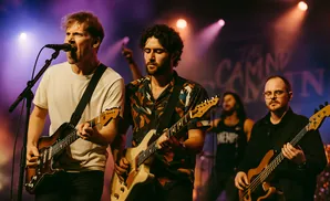 Band performing live on stage with purple and pink lighting.