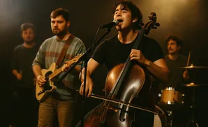 A band performs live, with a cellist singing into a microphone and guitarists and drummer visible.
