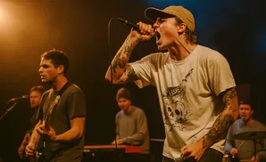 A band performs on stage with a singer in the foreground and guitarist behind him.