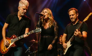 A band plays on stage, with a male guitarist on the left, a female singer in the middle, and a male guitarist on the right.