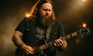 A bearded man with long hair plays an electric guitar on stage.