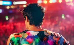 Rear view of a person in a colorful floral shirt on stage with a crowd in the background.