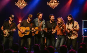 A band performs on stage, with a banjo player, two guitarists, a fiddler, and a mandolin player.