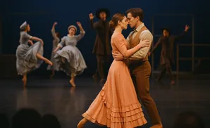 A ballet couple dances closely on stage, while other dancers perform in the background.