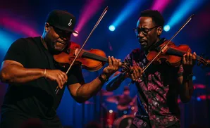Two Black men play violins on a stage with colorful lighting.