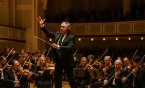 Conductor leading an orchestra, with violinists in the foreground playing.