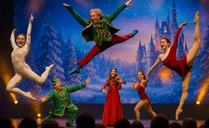 Dancers in festive costumes perform on stage with a winter castle backdrop.