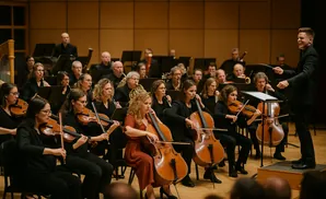 An orchestra performs, with a conductor directing string musicians playing violins and cellos.