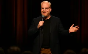 A man with glasses and red beard holds a microphone and speaks on stage.