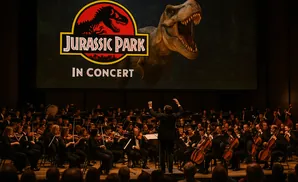 An orchestra performs Jurassic Park in concert with a T-Rex on screen.
