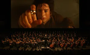 An orchestra performs in front of a screen showing Frodo Baggins holding the One Ring.