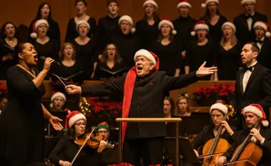 A choir and orchestra perform holiday music, many wearing Santa hats. A conductor leads the performance.