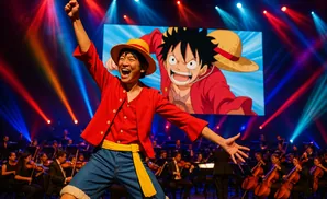 A performer dressed as Monkey D. Luffy from One Piece with a straw hat and red shirt on stage with a symphony orchestra.