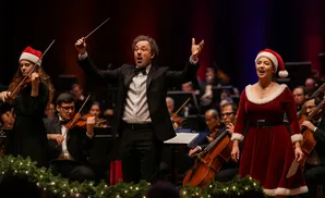 A conductor leads a Christmas concert with a singer and orchestra.