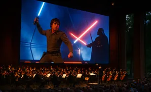 An orchestra performs live to a Star Wars movie projected on a large screen.