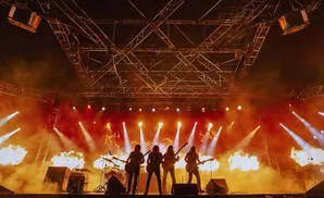 A rock band performs on stage with pyrotechnics and stage lighting.