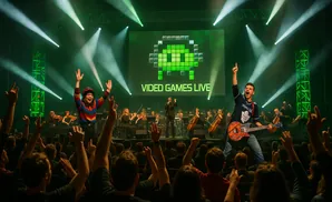 A rock guitarist and a female singer perform with an orchestra at Video Games Live, with a Space Invader logo on the screen.