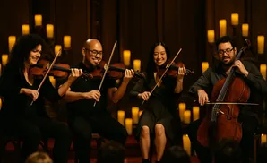 A string quartet performs by candlelight, with three violins and one cello.
