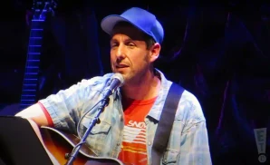adam sandler performing on stage while playing the acoustic guitar