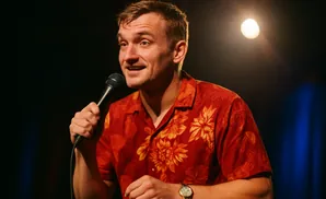 A man in a red floral shirt holds a microphone on stage.