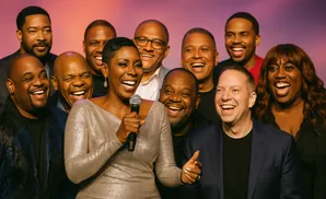 A diverse group of ten singers laughs joyfully while posing for a photo.