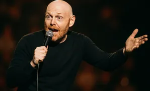 Bald man with a beard holding a microphone and gesturing with his hand while speaking on stage.