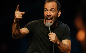 A man points with his left hand while holding a microphone with his right.