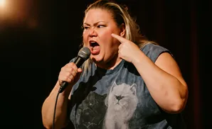 A woman performs on stage, singing into a microphone and pointing to her cheek.