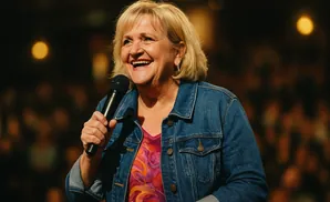 A woman with blonde hair smiles as she holds a microphone.
