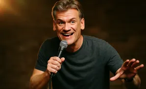 A man with a microphone smiles and gestures with his hand.