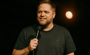 Man with beard holding a microphone, smiling.