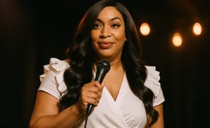 Woman in a white top holding a microphone, with blurred lights in the background.
