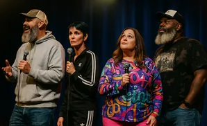 Four people on stage with microphones. Two men and two women, all wearing casual clothes.