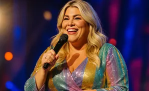 A blonde woman in a sequined dress holds a microphone and smiles.