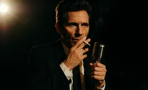 A man in a suit holds a cigarette and a vintage microphone, with smoke rising.