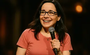 A smiling woman with glasses and black hair holds a microphone.
