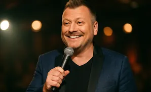 A man in a suit holding a microphone smiles broadly at a crowd.