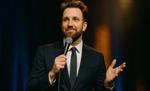 A man in a suit holds a microphone and gestures with his hand while speaking.