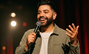 A man holds a microphone and gestures with his hand, smiling.