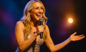 A woman with blonde hair laughs into a microphone on a stage.